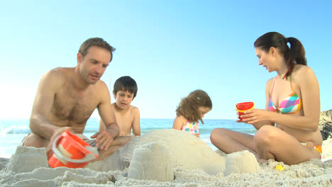 Glückliche-Eltern-Bauen-Mit-Ihren-Kindern-Eine-Sandburg
