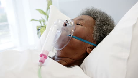 African-american-senior-female-patient-with-oxygen-mask-lying-in-bed-in-hospital-room,-slow-motion