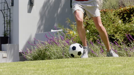 Low-section-of-biracial-man-practicing-football-skills-in-sunny-garden,-slow-motion
