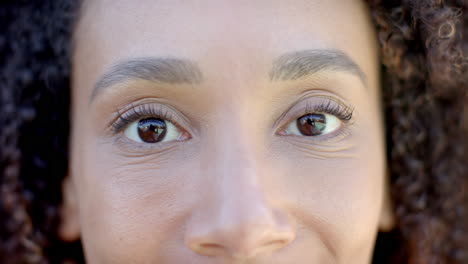 Portrait-close-up-of-brown-eyes-of-happy-biracial-woman-with-curly-hair-smiling-in-sun,-slow-motion