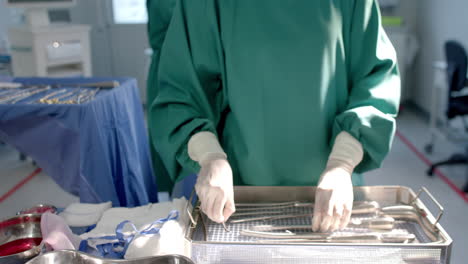 Portrait-of-biracial-female-surgeon-sorting-surgical-tools-in-theatre,-copy-space,-slow-motion