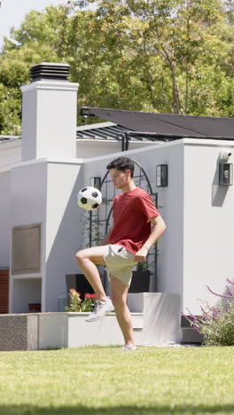 Vertical-video-of-biracial-man-practicing-football-skills-in-sunny-garden,-slow-motion