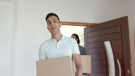 Happy-diverse-gay-male-couple-moving-into-new-home,-carrying-boxes,-slow-motion