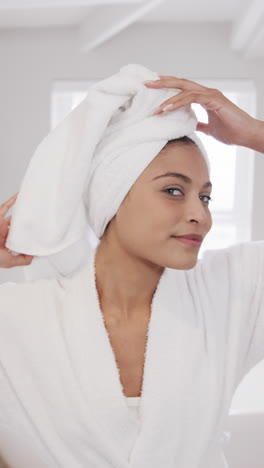 Vertical-video-of-portrait-of-happy-biracial-woman-wearing-towel-on-head-in-bathroom,-slow-motion