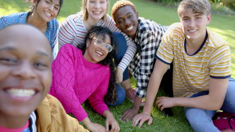 Happy-diverse-group-of-teenage-friends-sitting-on-grass-and-embracing-in-sunny-park,-slow-motion