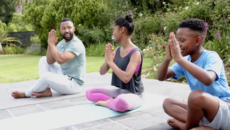 Padre-Afroamericano-Enseñando-Meditación-De-Yoga-A-Hijo-E-Hija-Sentados-En-El-Jardín,-Cámara-Lenta