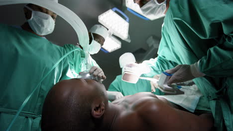 Diverse-surgeons-using-defibrillator-on-patient-in-operating-theatre-at-hospital,-slow-motion