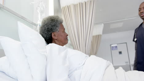 Happy-african-american-male-doctor-talking-with-female-senior-patient-in-hospital-room,-slow-motion