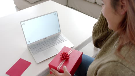 Happy-plus-size-biracial-woman-with-gift-having-laptop-video-call,-copy-space-on-screen,-slow-motion