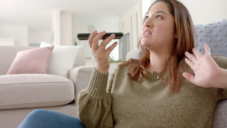 Happy-plus-size-biracial-woman-relaxing-in-living-room-talking-on-smartphone,-slow-motion