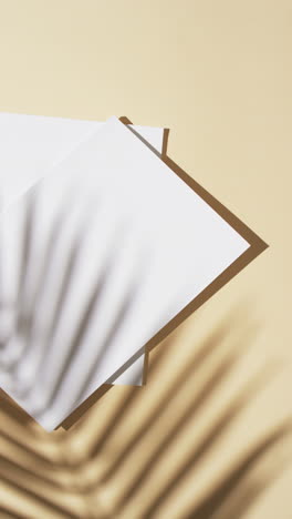 Vertical-video-of-shadow-of-plant-over-books-with-blank-pages-and-copy-space-on-yellow-background