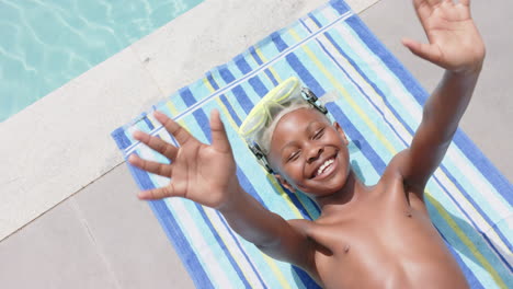 Hoher-Winkel-Eines-Glücklichen-Afroamerikanischen-Jungen-Mit-Schutzbrille-Beim-Sonnenbaden,-Winken-Am-Pool,-Zeitlupe