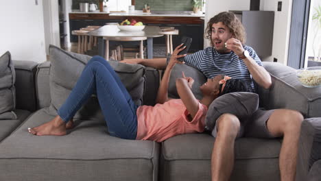 Diverse-couple,-a-young-African-American-woman-and-a-young-Caucasian-man,-relax-on-a-sofa-at-home