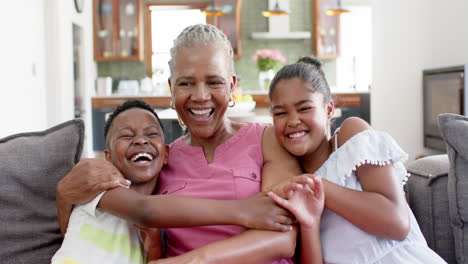 Happy-african-american-grandchildren-and-grandmother-embracing,-laughing-on-sofa,-slow-motion