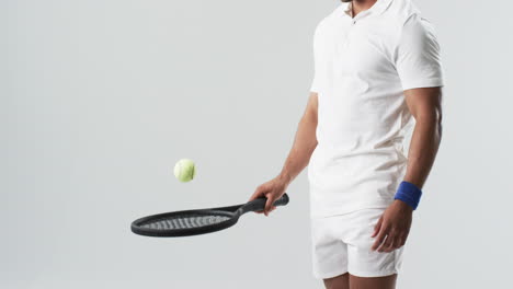 Young-biracial-man-in-tennis-attire-plays-with-a-ball,-with-copy-space
