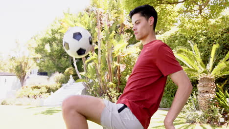 Focused-biracial-man-juggling-football-with-thighs-in-sunny-garden,-copy-space,-slow-motion