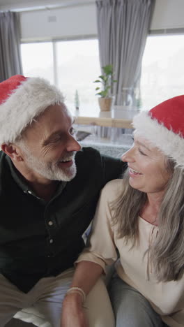 Vertical-video-of-happy-senior-caucasian-couple-wearing-santa-hats-having-video-call,-slow-motion