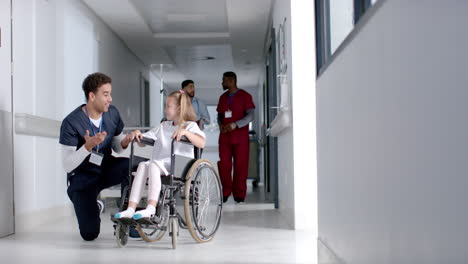 Young-biracial-male-nurse-assists-a-Caucasian-girl-in-a-wheelchair-at-a-hospital