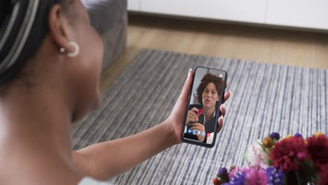 Biracial-woman-holding-smartphone-with-biracial-man-with-flower-on-screen