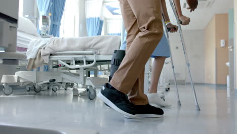 Low-section-of-diverse-male-doctor-helping-female-patient-using-crutches,-copy-space,-slow-motion