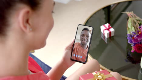 Caucasian-woman-holding-gift-and-smartphone-with-african-emerican-man-on-screen