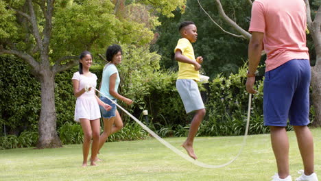 Glückliche-Afroamerikanische-Eltern,-Sohn-Und-Tochter-Hüpfen-Im-Sonnigen-Garten,-Zeitlupe