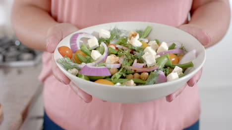 Midsection-of-plus-size-biracial-woman-holding-bowl-of-feta-salad,-slow-motion
