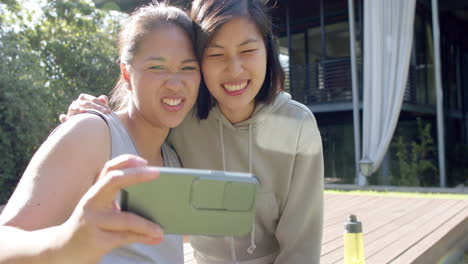 Glückliche-Asiatische-Freundinnen-Mit-Wasserflasche-Machen-Selfie-Und-Machen-Grimassen-Auf-Der-Terrasse,-Zeitlupe