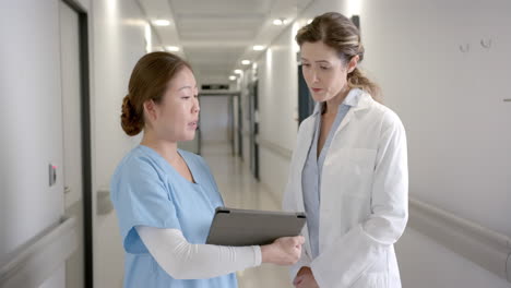 Portrait-of-happy-diverse-female-doctors-with-tablet-discussing-in-hospital-corridor,-slow-motion