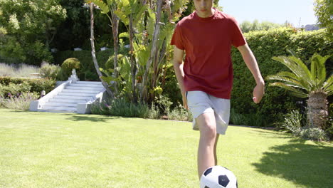 Focused-biracial-man-practicing-skills-with-football-in-sunny-garden,-copy-space,-slow-motion