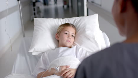 A-young-Caucasian-girl-lies-in-a-hospital-bed,-talking-to-a-nurse