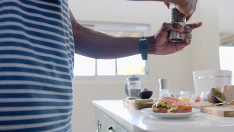 African-american-man-seasoning-avocado-toasts-in-sunny-kitchen,-slow-motion
