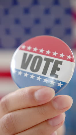 Vertical-video-of-hand-of-biracial-teenage-girl-holding-american-vote-badge,-copy-space,-slow-motion