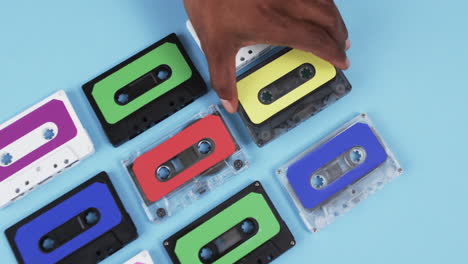 Video-of-african-american-man's-hand-arranging-retro-tapes-with-copy-space-on-blue-background