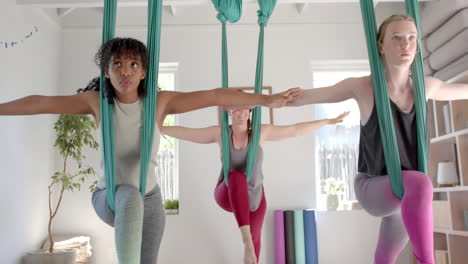 Focused-diverse-fitness-teenage-girls-exercising-in-aerial-yoga-class-in-big-white-room,-slow-motion