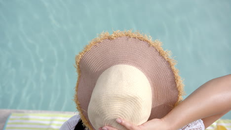Biracial-teenage-girl-in-sunhat-sitting-by-sunny-swimming-pool,-slow-motion