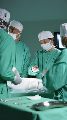 Vertical-video-of-diverse-surgeons-operating-on-patient-in-operating-theatre,-slow-motion