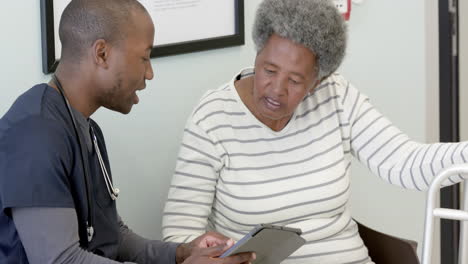 African-american-male-doctor-using-tablet-and-talking-with-senior-woman-in-hospital,-slow-motion