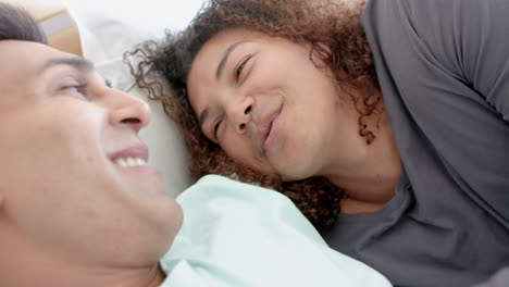 Happy-diverse-gay-male-couple-lying-on-bed-smiling-and-talking-at-home,-slow-motion