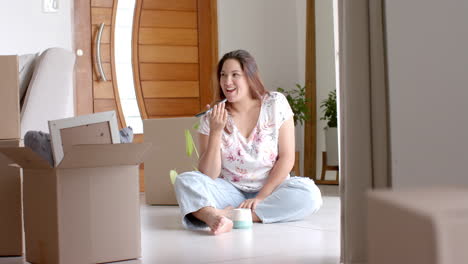 Happy-plus-size-biracial-woman-talking-on-phone-on-floor-of-new-home,-copy-space,-slow-motion