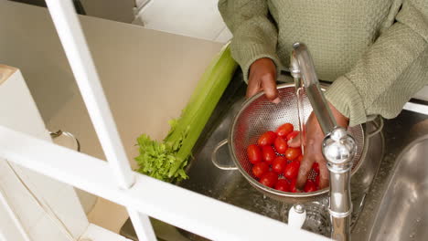 Hands-of-african-american-senior-woman-washing-tomatoes-in-sunny-kitchen,-slow-motion