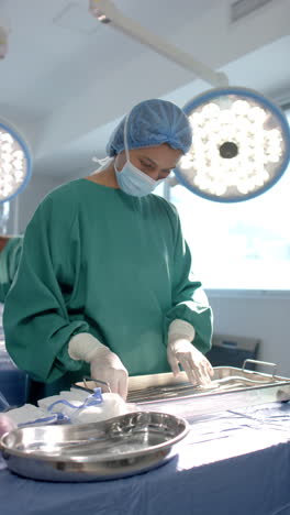 Vertical-video-of-biracial-female-surgeon-preparing-surgical-instruments-in-theatre,-slow-motion