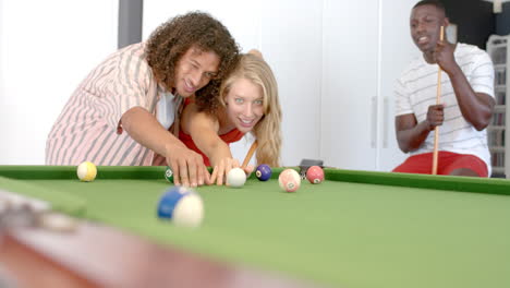 Biracial-man-teaches-young-Caucasian-woman-to-play-pool,-with-copy-space