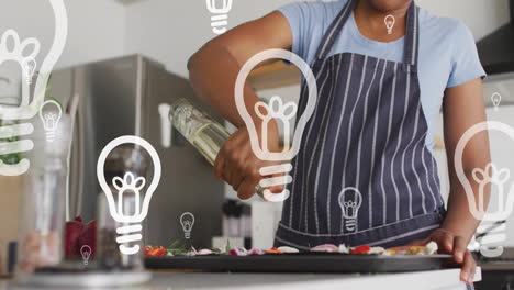 Animation-of-lightbulbs-over-afrcian-american-woman-preparing-food-in-kitchen