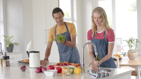 Happy-diverse-couple-cooking-and-throwing-waste-out-in-kitchen,-slow-motion