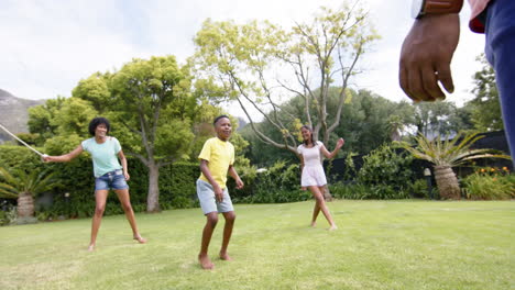 Happy-african-american-parents,-son-and-daughter-skipping-in-sunny-garden,-slow-motion