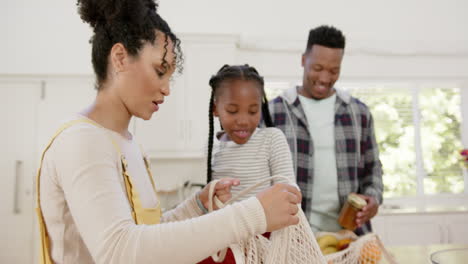 Felices-Padres-Afroamericanos-E-Hija-Desempacando-Bolsas-De-Compras-En-Casa,-Cámara-Lenta
