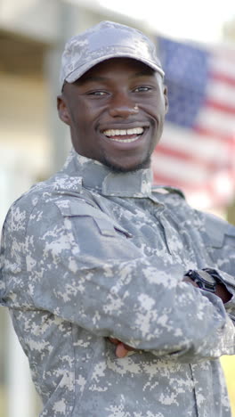 Glücklicher-Afroamerikanischer-Soldat,-Der-An-Einem-Sonnigen-Tag-Mit-Der-Flagge-Im-Hintergrund-Steht,-Zeitlupe