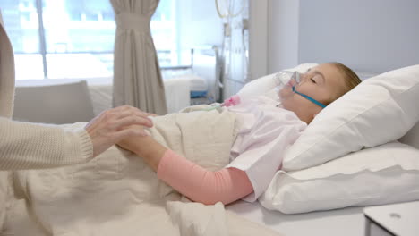 Midsection-of-caucasian-mother-holding-hand-of-daughter-patient-in-hospital-bed,-slow-motion