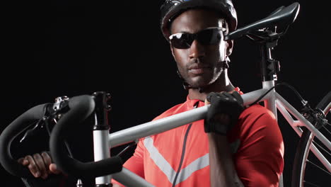 Focused-African-American-cyclist-holding-a-bicycle-on-a-black-background